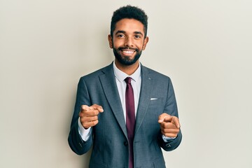 Handsome hispanic man with beard wearing business suit and tie pointing fingers to camera with happy and funny face. good energy and vibes.