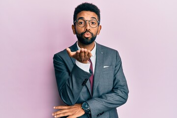 Handsome hispanic business man with beard wearing business suit and tie looking at the camera blowing a kiss with hand on air being lovely and sexy. love expression.