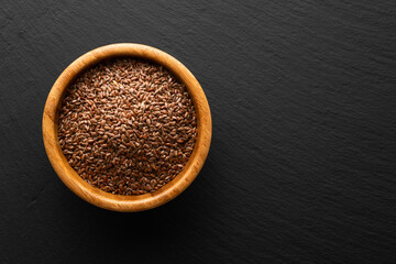 flax seeds in a wooden bowl on a slate background, top view