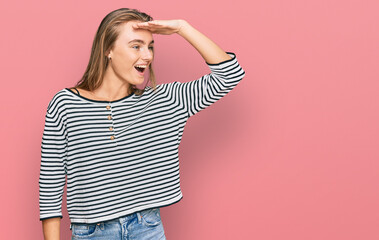 Beautiful blonde woman wearing casual clothes very happy and smiling looking far away with hand over head. searching concept.