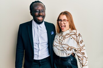 Young interracial couple wearing business and elegant clothes winking looking at the camera with sexy expression, cheerful and happy face.