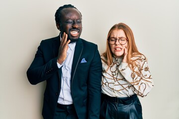 Young interracial couple wearing business and elegant clothes touching mouth with hand with painful expression because of toothache or dental illness on teeth. dentist concept.