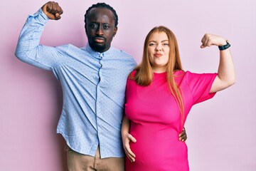 Young interracial couple expecting a baby, touching pregnant belly strong person showing arm muscle, confident and proud of power