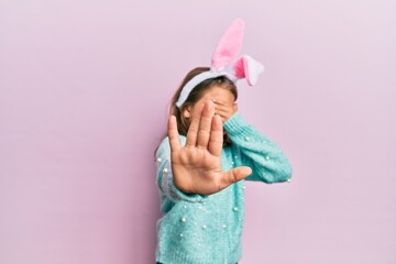 Little beautiful girl wearing cute easter bunny ears covering eyes with hands and doing stop gesture with sad and fear expression. embarrassed and negative concept.