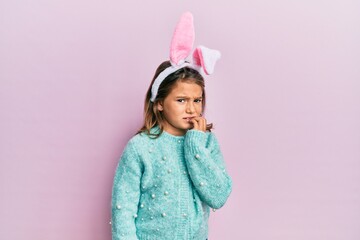 Little beautiful girl wearing cute easter bunny ears looking stressed and nervous with hands on...