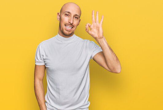 Bald man with beard wearing casual white t shirt smiling positive doing ok sign with hand and fingers. successful expression.