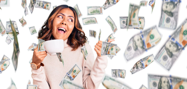 Young beautiful mixed race woman holding a cup of coffee pointing thumb up to the side smiling happy with open mouth