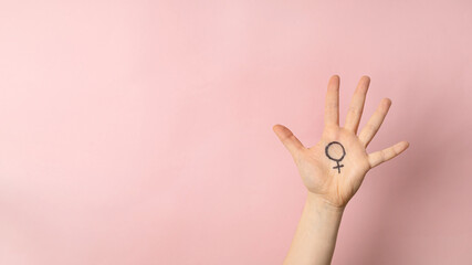 Female hand with female symbol of Venus on pink background for international womens day