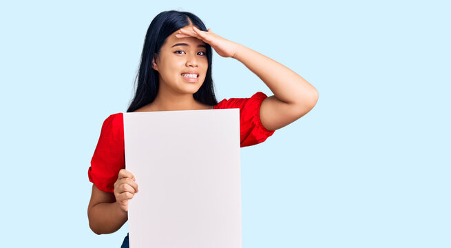 Young beautiful asian girl holding blank empty banner stressed and frustrated with hand on head, surprised and angry face