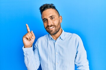 Handsome man with beard wearing casual clothes showing and pointing up with finger number one while smiling confident and happy.