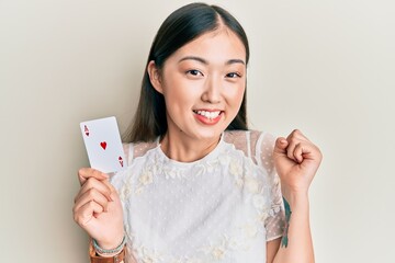 Young chinese woman holding ace poker card screaming proud, celebrating victory and success very...