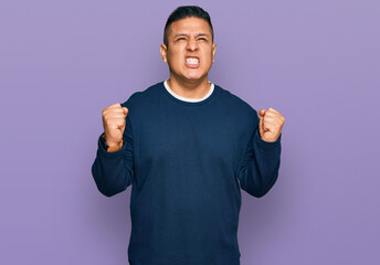 Young latin man wearing casual clothes crazy and mad shouting and yelling with aggressive expression and arms raised. frustration concept.