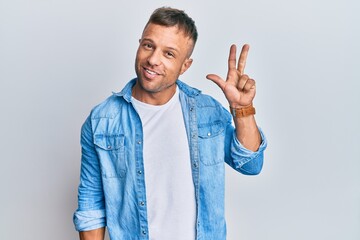 Handsome muscle man wearing casual denim jacket showing and pointing up with fingers number three while smiling confident and happy.