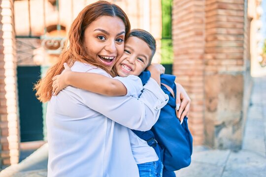 Adorable latin student boy and mom hugging at the city.