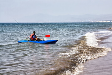 Man fishing in a kayak in the sea. Fisherman kayaking in the Mediterranean sea