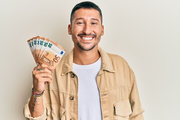 Handsome man with tattoos holding 50 euro banknotes looking positive and happy standing and smiling with a confident smile showing teeth - obrazy, fototapety, plakaty