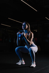 Attractive muscular sexy woman doing squats with kettlebell in the gym.