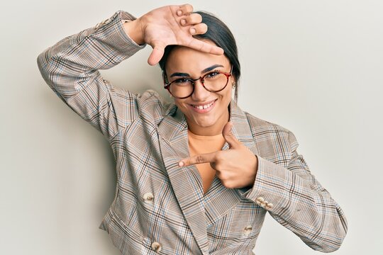 Young brunette woman wearing business jacket and glasses smiling making frame with hands and fingers with happy face. creativity and photography concept.