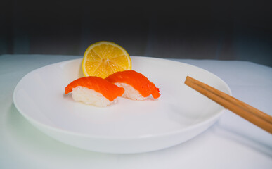 side view, on a gray and white background, a white plate with sushi and lemon, on rice-red fish, on a plate are chopsticks