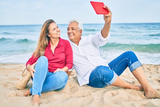Middle age hispanic couple smiling happy making selfie by the tablet at the beach.