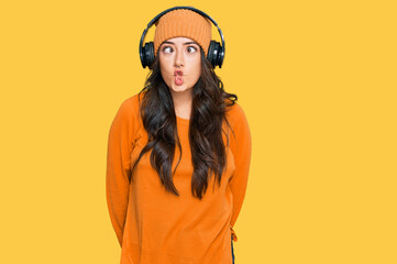 Beautiful brunette young woman listening to music using headphones making fish face with lips, crazy and comical gesture. funny expression.