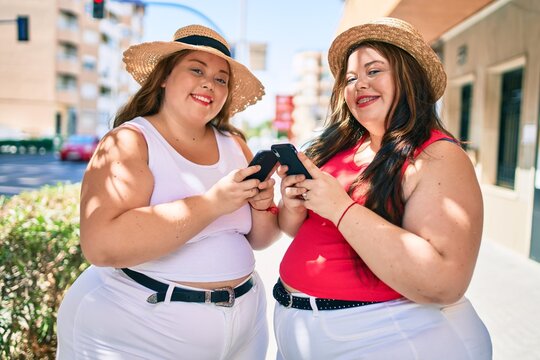 Two plus size overweight sisters twins women with smartphone outdoors on a sunny day