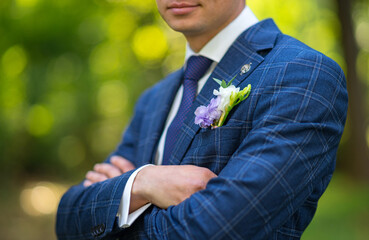 Naklejka na ściany i meble close-up of the groom in a blue suit with a boutaniere against the backdrop of a green garden.