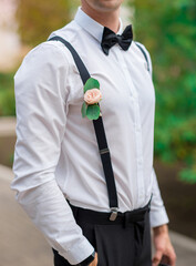 butaniere of eucalyptus leaves and rosebud on the chest of the groom in a white shirt and bow tie