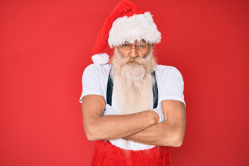 Old senior man with grey hair and long beard wearing white t-shirt and santa claus costume skeptic...