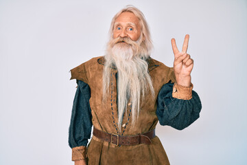 Old senior man with grey hair and long beard wearing viking traditional costume showing and pointing up with fingers number two while smiling confident and happy.