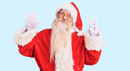 Old senior man with grey hair and long beard wearing traditional santa claus costume showing and pointing up with fingers number eight while smiling confident and happy.