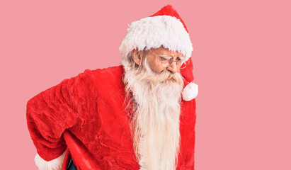 Old senior man with grey hair and long beard wearing traditional santa claus costume suffering of...
