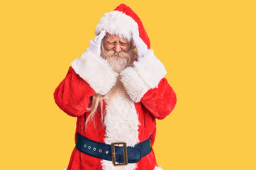 Old senior man with grey hair and long beard wearing traditional santa claus costume with hand on head, headache because stress. suffering migraine.