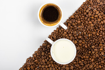 A cup of coffee and a cup of milk standing on coffee beans scattered on a white background.