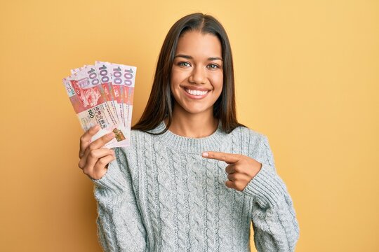 Beautiful hispanic woman holding 100 hong kong dollars banknotes smiling happy pointing with hand and finger
