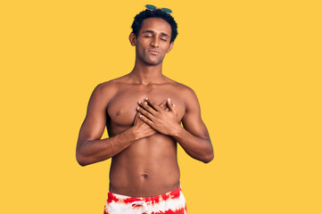 Fototapeta premium African handsome man wearing swimsuit and sunglasses smiling with hands on chest with closed eyes and grateful gesture on face. health concept.