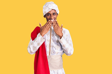 African handsome man wearing tradition sherwani saree clothes laughing and embarrassed giggle covering mouth with hands, gossip and scandal concept