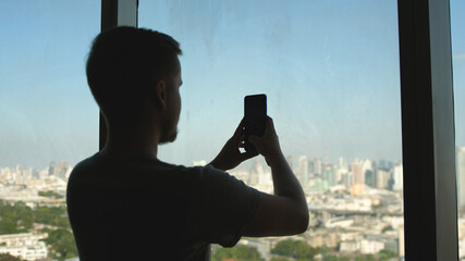 Handsome businessman by the window uses the phone taking picture in Office City View