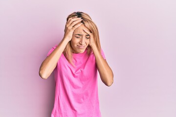 Beautiful blonde woman wearing casual pink tshirt suffering from headache desperate and stressed because pain and migraine. hands on head.