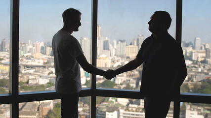 Fototapeta na wymiar Businessmen meeting in front of panoramic window. They are shaking hands and discussing work