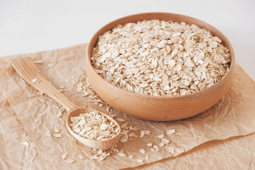 Dry oatmeal in a wooden plate and spoon on kraft paper on a white background. Top view. Copy, empty space for text