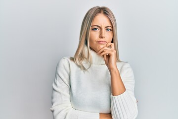 Beautiful blonde woman wearing casual turtleneck sweater thinking concentrated about doubt with...
