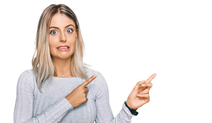 Beautiful blonde woman wearing casual clothes pointing aside worried and nervous with both hands,...