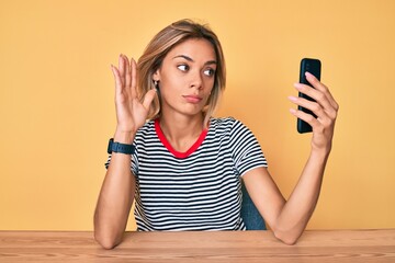 Beautiful caucasian woman doing video call waving to smartphone relaxed with serious expression on face. simple and natural looking at the camera.