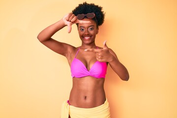 Young african american woman wearing bikini smiling making frame with hands and fingers with happy face. creativity and photography concept.