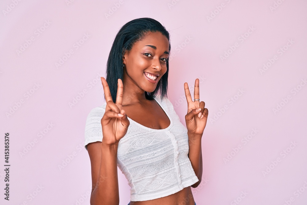 Wall mural young african american woman wearing casual clothes smiling looking to the camera showing fingers do