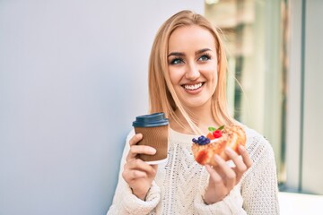 Young blonde girl smiling happy having breakfast standing at the city.