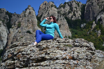 Naklejka na ściany i meble Girl sitting on a rock in sunglasses against the backdrop of mountains