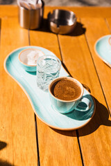 a cup of hot black turkish coffee in blue cup served with glass of water and sugar