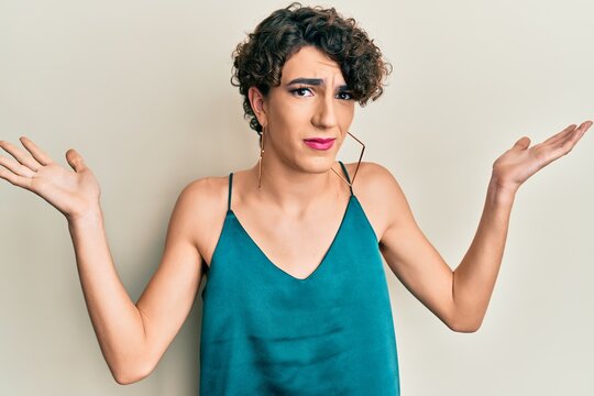 Young man wearing woman make up wearing party clothes clueless and confused with open arms, no idea and doubtful face.